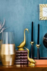 Stylish home decor arrangement including a globe, books, candles, and vases on a blue backdrop.